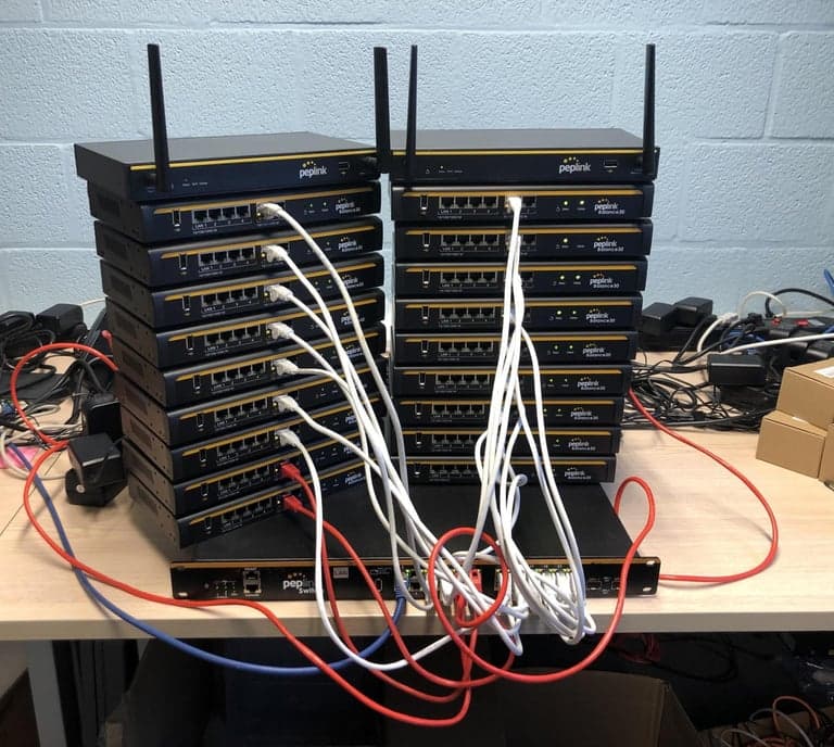 Stacks of Peplink Balance routers wired to a Peplink switch on a workbench